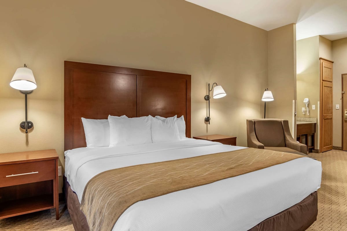 Une chambre d’hôtel avec un grand lit, deux tables de chevet, une chaise, un miroir et des lampes fixées au mur.