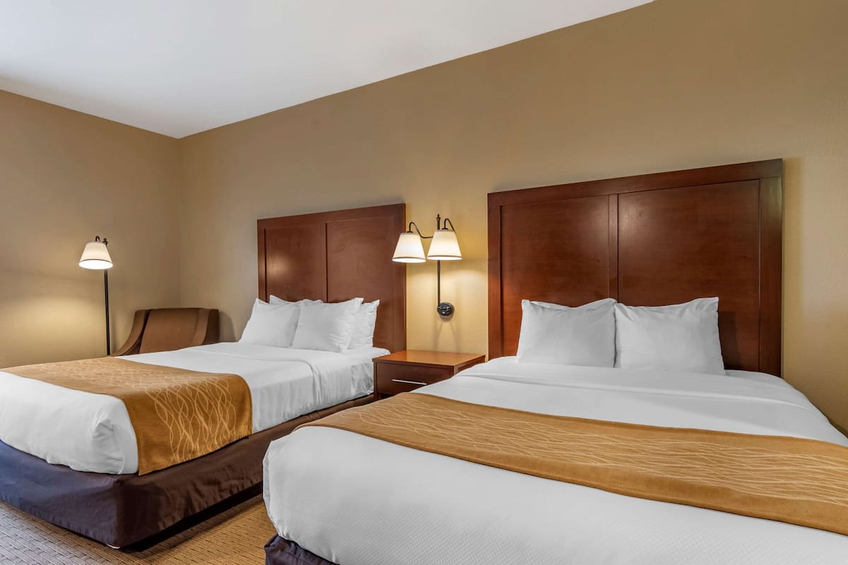 Une chambre d’hôtel avec deux lits, des têtes de lit en bois, des tables de chevet avec des lampes et un sol recouvert de moquette.