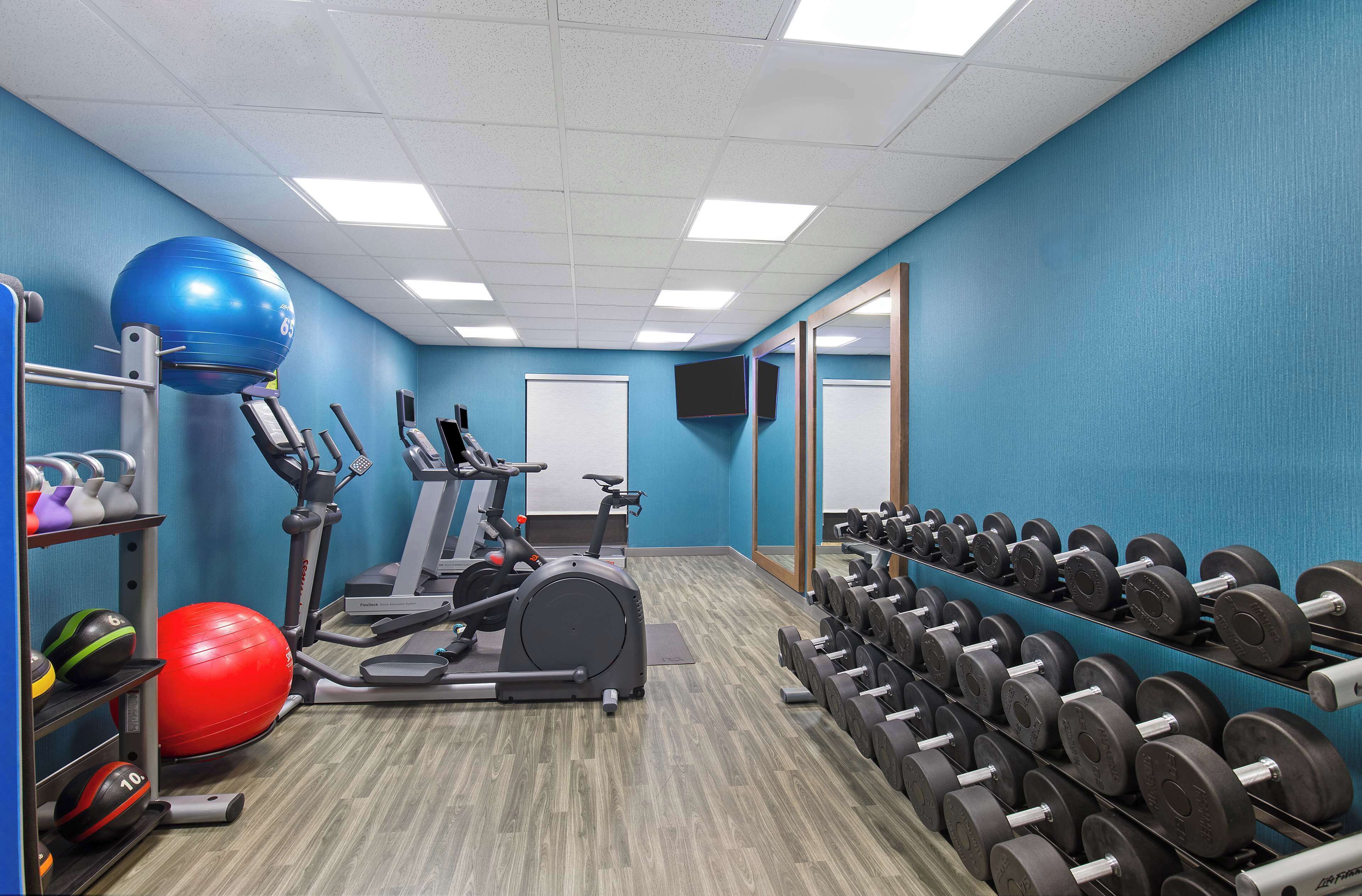 Un gimnasio con cintas de correr, una máquina elíptica, una pelota de ejercicio roja y un estante con mancuernas.