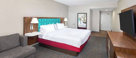 A hotel room with a bed, a sofa, a desk, a TV, and a bathroom visible through an open door.