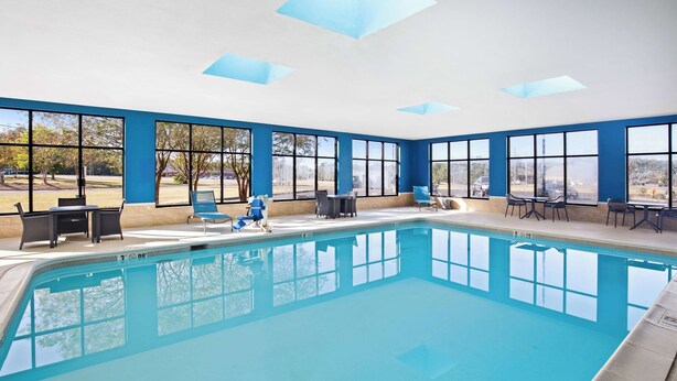 Une piscine intérieure à l’eau d’un bleu cristallin, entourée de grandes fenêtres qui offrent une vue sur les arbres et un paysage lointain.