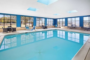 Una piscina interior con agua cristalina y azul, rodeada de amplias ventanas que ofrecen vistas a árboles y un paisaje lejano.