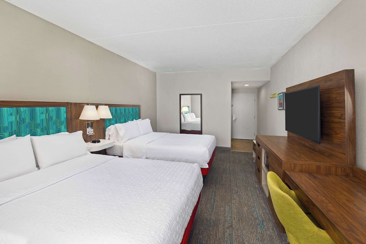 Quarto de hotel com duas camas, uma mesa, televisão e espelho.