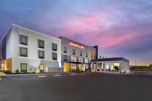 Un hotel Hampton Inn con un diseño moderno, un espacio exterior cubierto y un estacionamiento.