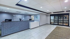 Un espace d’accueil au design moderne, comprenant un comptoir de réception, un panneau d’accueil et une vue à travers une porte vitrée.