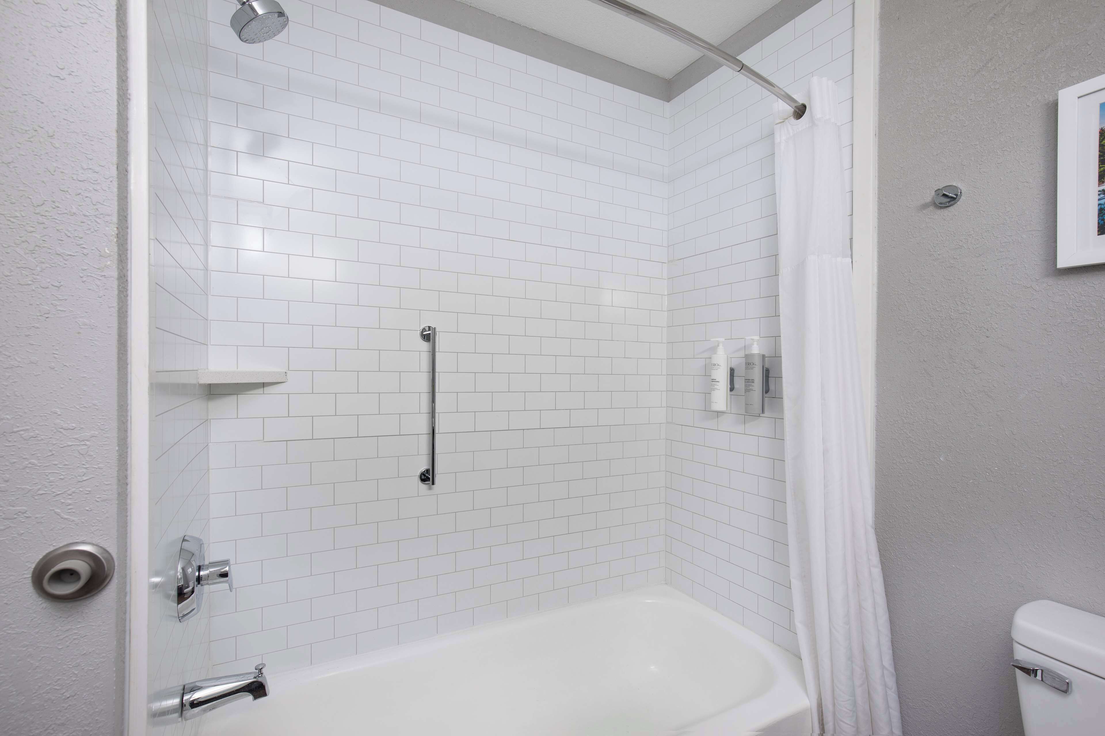 A bathroom with white tiled walls, a white bathtub, a shower with a curtain, and a toilet.