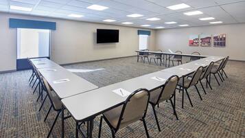 A conference room with a long table, chairs, a flat-screen TV, windows, and artwork on the wall.
