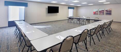 A conference room with a long table, chairs, a flat-screen TV, windows, and artwork on the wall.
