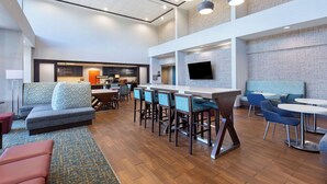 Un hall d’hôtel moderne doté d’un bar, de coins salon et d’un téléviseur à écran plat fixé au mur.