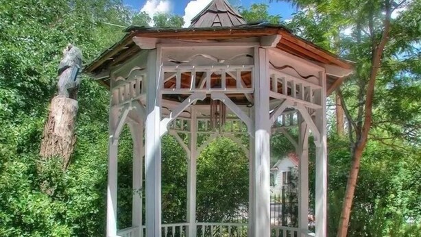 A gazebo with a white frame and a red roof, surrounded by greenery and a stone wall. - Spurs n Lace Bed & Breakfast Inn (Colorado Springs)