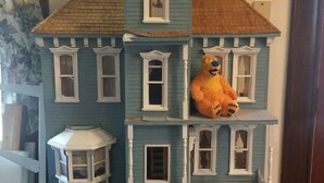 A dollhouse with a bear figure on the second floor, a lantern on the ground floor, and a blue and white exterior. - Spurs n Lace Bed & Breakfast Inn (Colorado Springs)