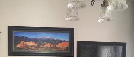 A dining area with a table set for four, framed landscape paintings on the wall, and a chandelier above.