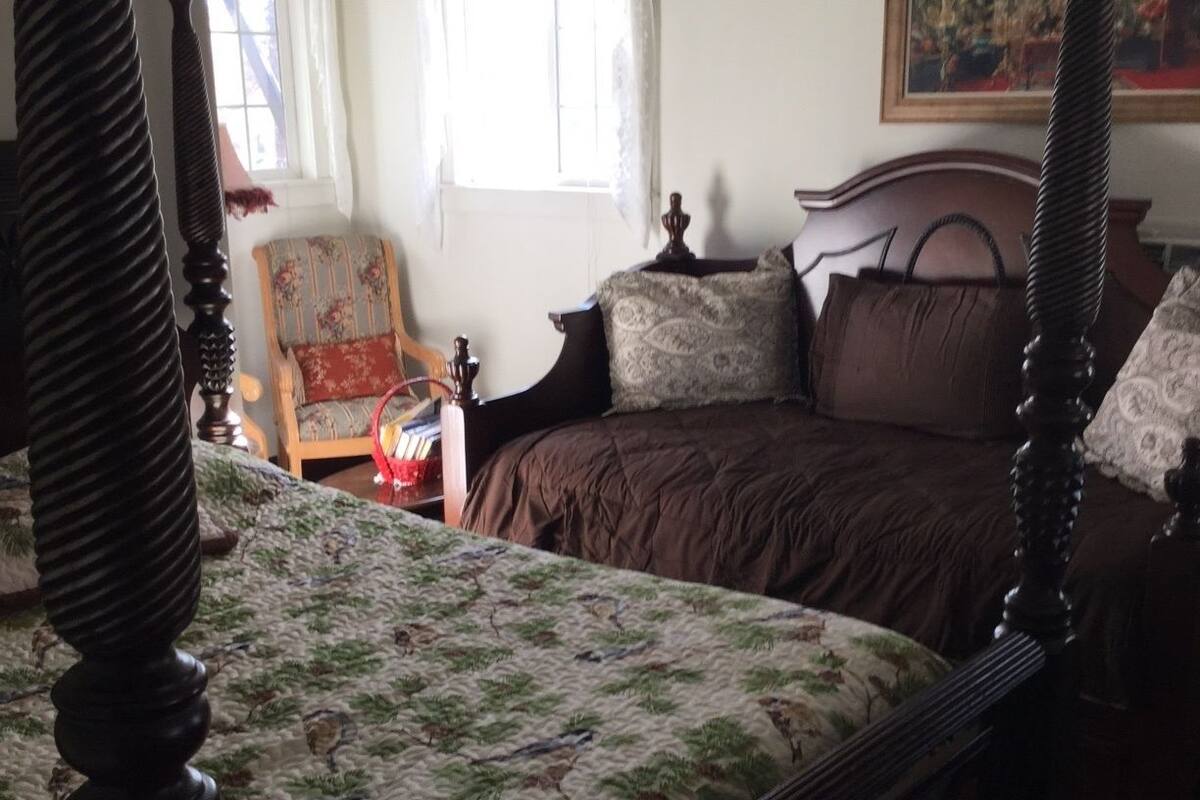 A bedroom with a four-poster bed, a chair, and a painting on the wall.