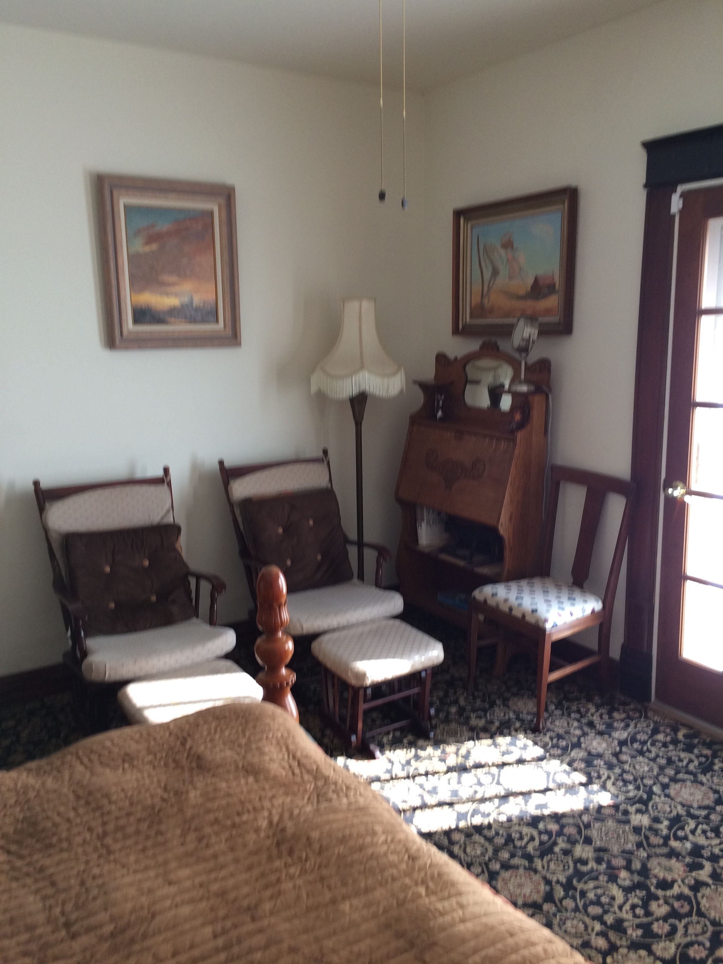 A room with a bed, two armchairs, a small table, a lamp, and two paintings on the wall.