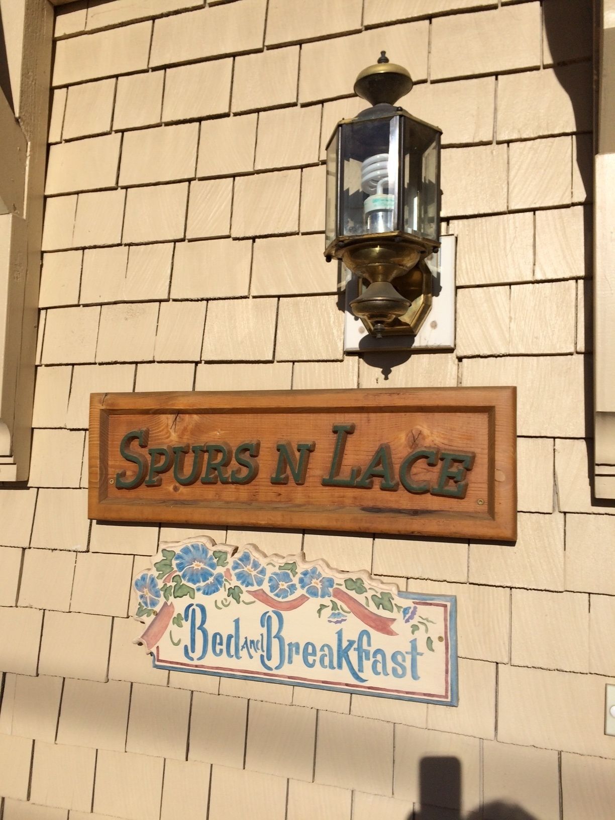 Ein Schild für 'Spurs N Lace Bed & Breakfast' mit dekorativem Rahmen und einer Laterne darüber.
