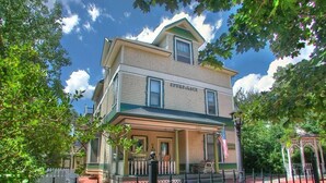 A two-story building with a porch, labeled "SPURS PLACE," featuring a brick facade and green trim. - Spurs n Lace Bed & Breakfast Inn (Colorado Springs)