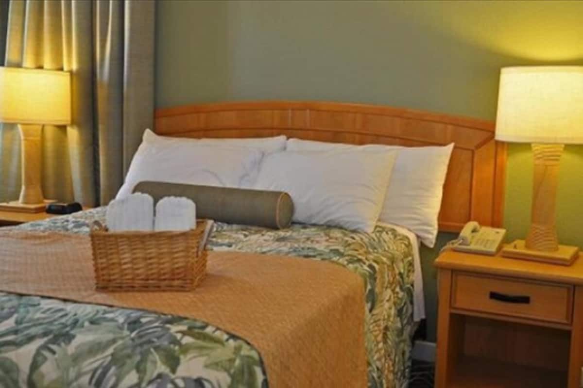 A hotel room with a bed, a nightstand with a lamp, a telephone, and a basket with towels.