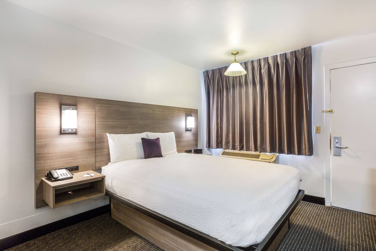 A hotel room with a large bed, bedside tables, a telephone, and a window with curtains.