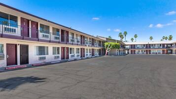 Un motel con varias habitaciones, estacionamiento y palmeras al fondo.