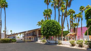 A hotel lobby with a 'Lobby' sign, palm trees, and a parking lot.