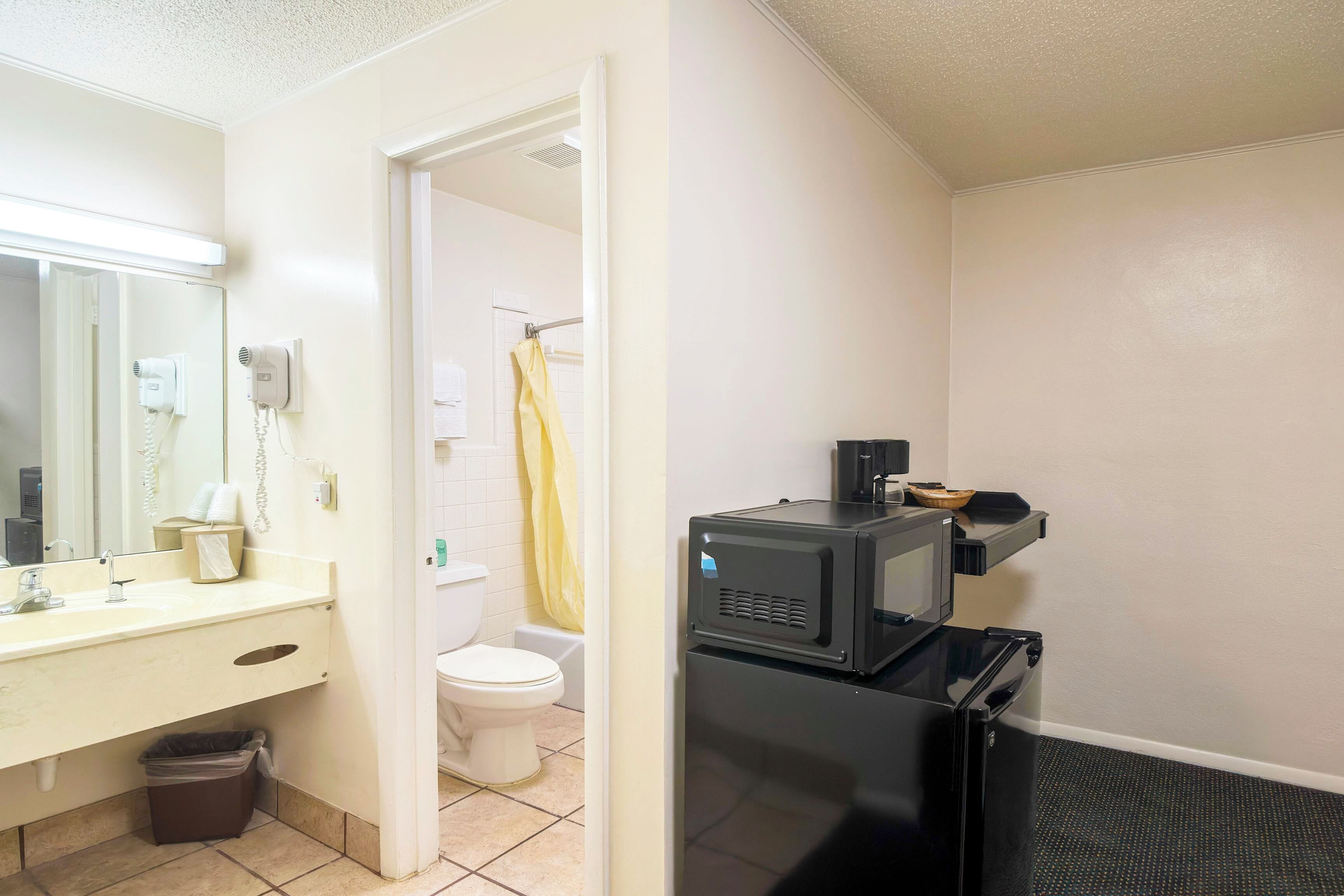 A compact bathroom with a sink, toilet, and a microwave.