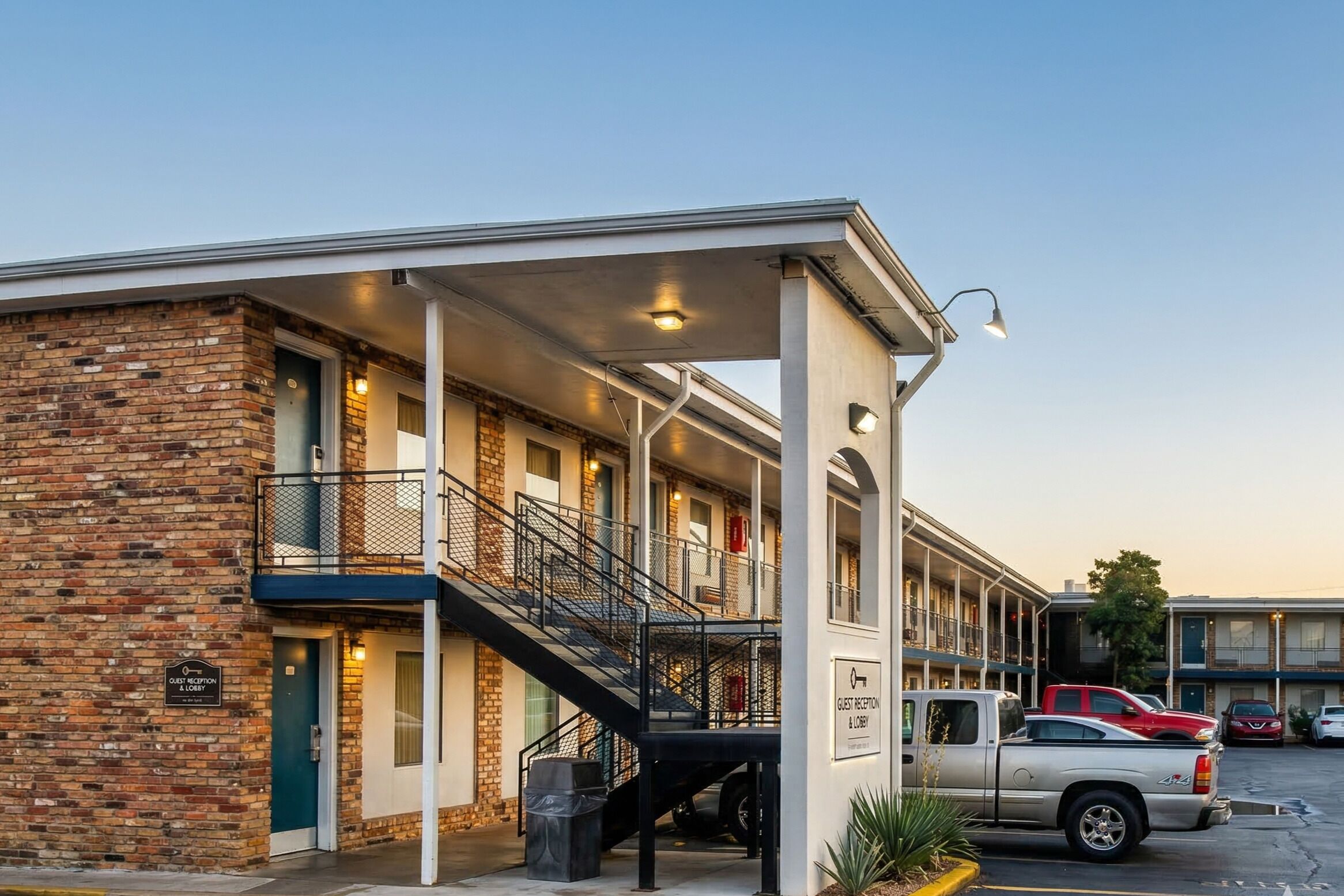 A hotel with a brick facade, a covered entrance, a staircase, and a parking lot.
