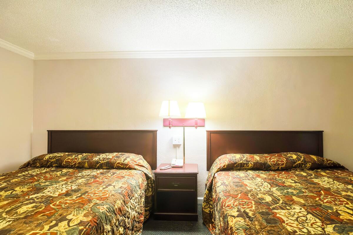 Ein Hotelzimmer mit zwei Einzelbetten, einem Nachttisch und einer Lampe dazwischen.