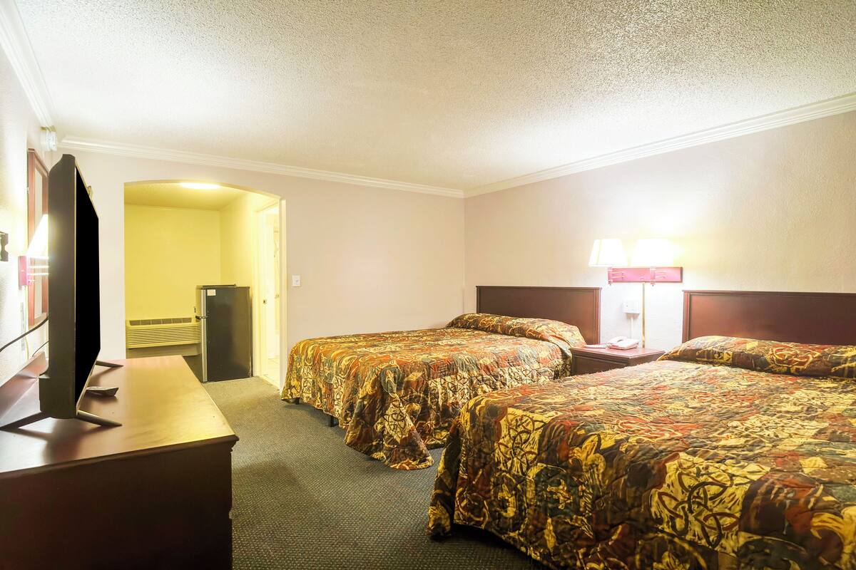 Ein Hotelzimmer mit zwei Betten, einem Schreibtisch, einem Fernseher und einer Lampe.