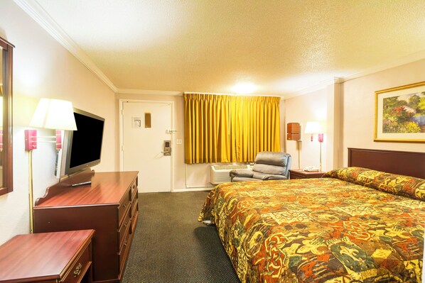 Habitación de hotel con cama, televisor, escritorio, silla y un cuadro en la pared.