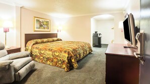 Ein Hotelzimmer mit einem großen Bett, einem Schreibtisch mit Fernseher, einem Sessel und einem Bild an der Wand.