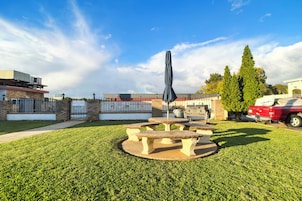 A courtyard with stone tables and an umbrella, surrounded by a well-maintained lawn and tall trees.