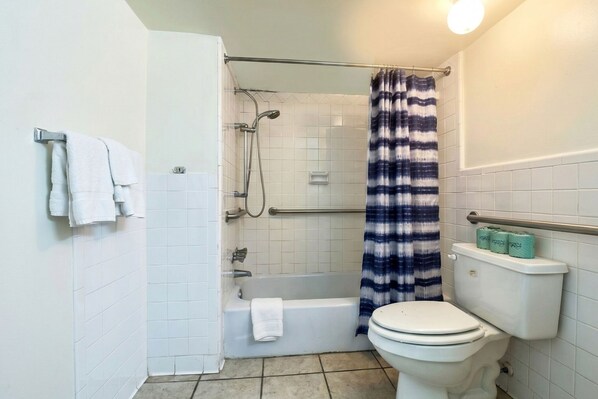 Un baño con bañera, ducha, inodoro y toallero con toallas.