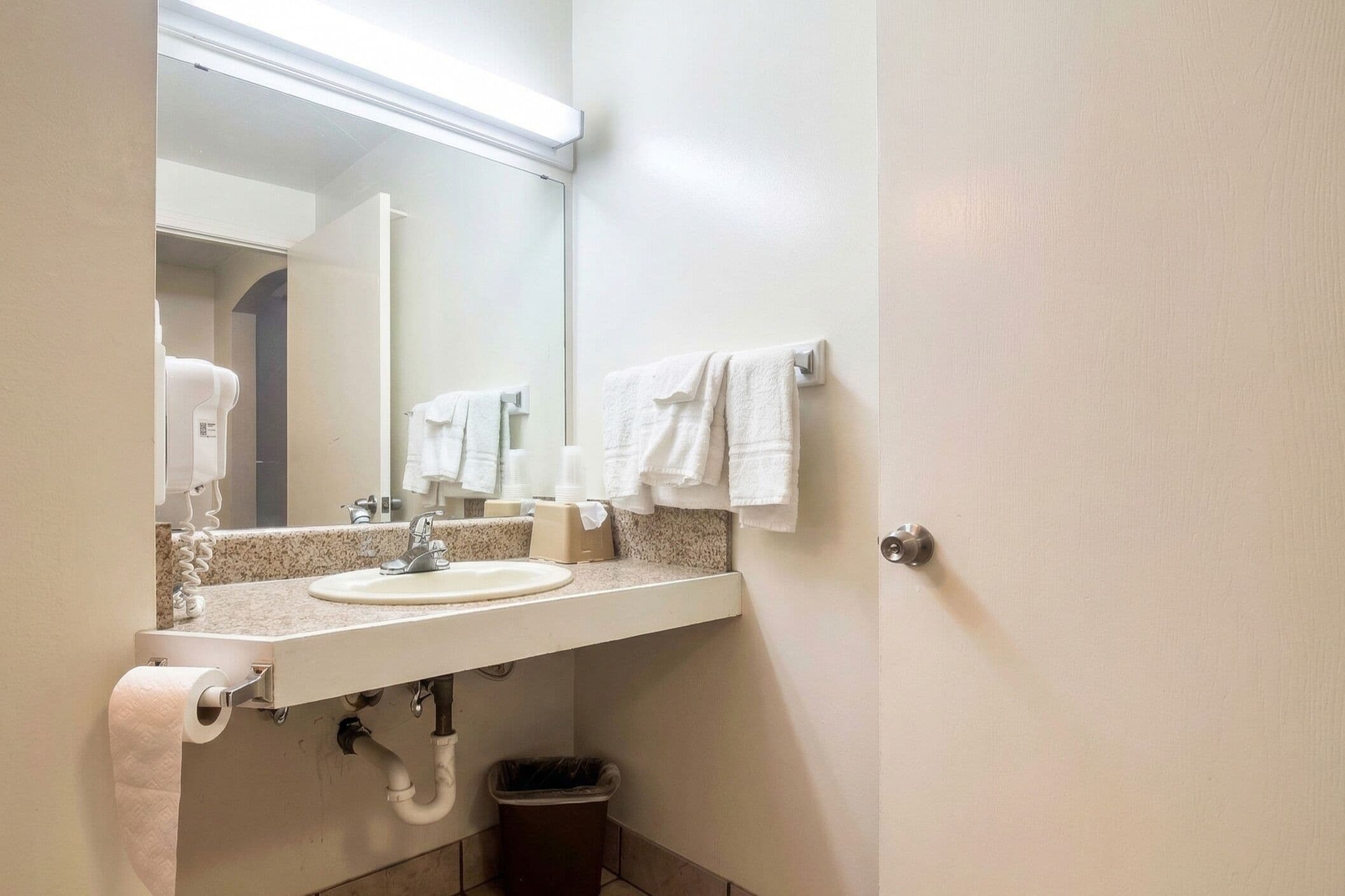 Un baño con lavamanos, espejo, toallero y un cubo de basura.