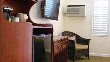 Una habitación de hotel compacta con kitchenette, televisión, una silla de mimbre y una ventana con persianas.