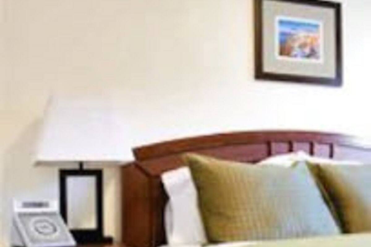 Quarto de hotel com uma cama, uma mesa de cabeceira com abajur, um quadro na parede e uma pequena mesa com telefone.