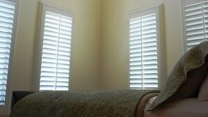 A bedroom with a bed, a ceiling light, and three windows with blinds. - Bella Capri Inn (Camarillo)