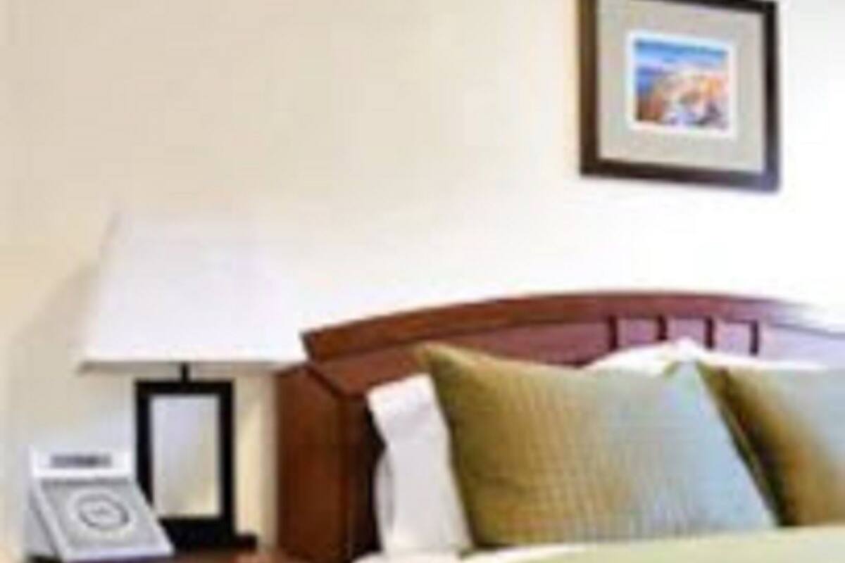 Quarto de hotel com uma cama, mesa de cabeceira com abajur e um quadro pendurado na parede.