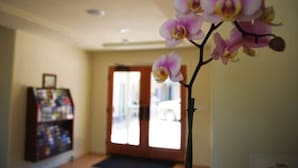 A hallway with a door, a small bookshelf, and an orchid plant. - Bella Capri Inn (Camarillo)