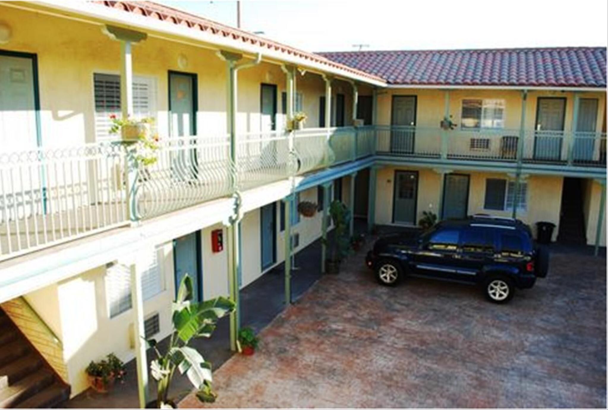 Un edificio a due piani con un balcone coperto e un'auto parcheggiata nel cortile.