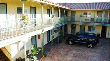 Un edificio a due piani con un balcone coperto e un'auto parcheggiata nel cortile.
