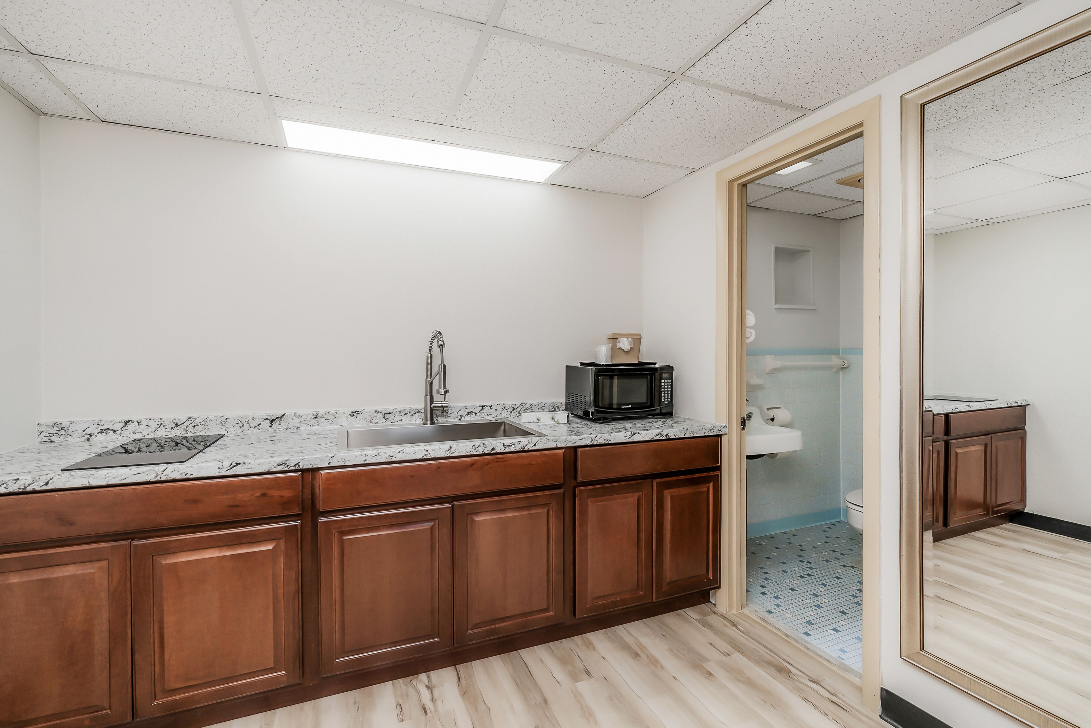 A kitchen with a marble countertop, wooden cabinets, a sink, and a microwave.