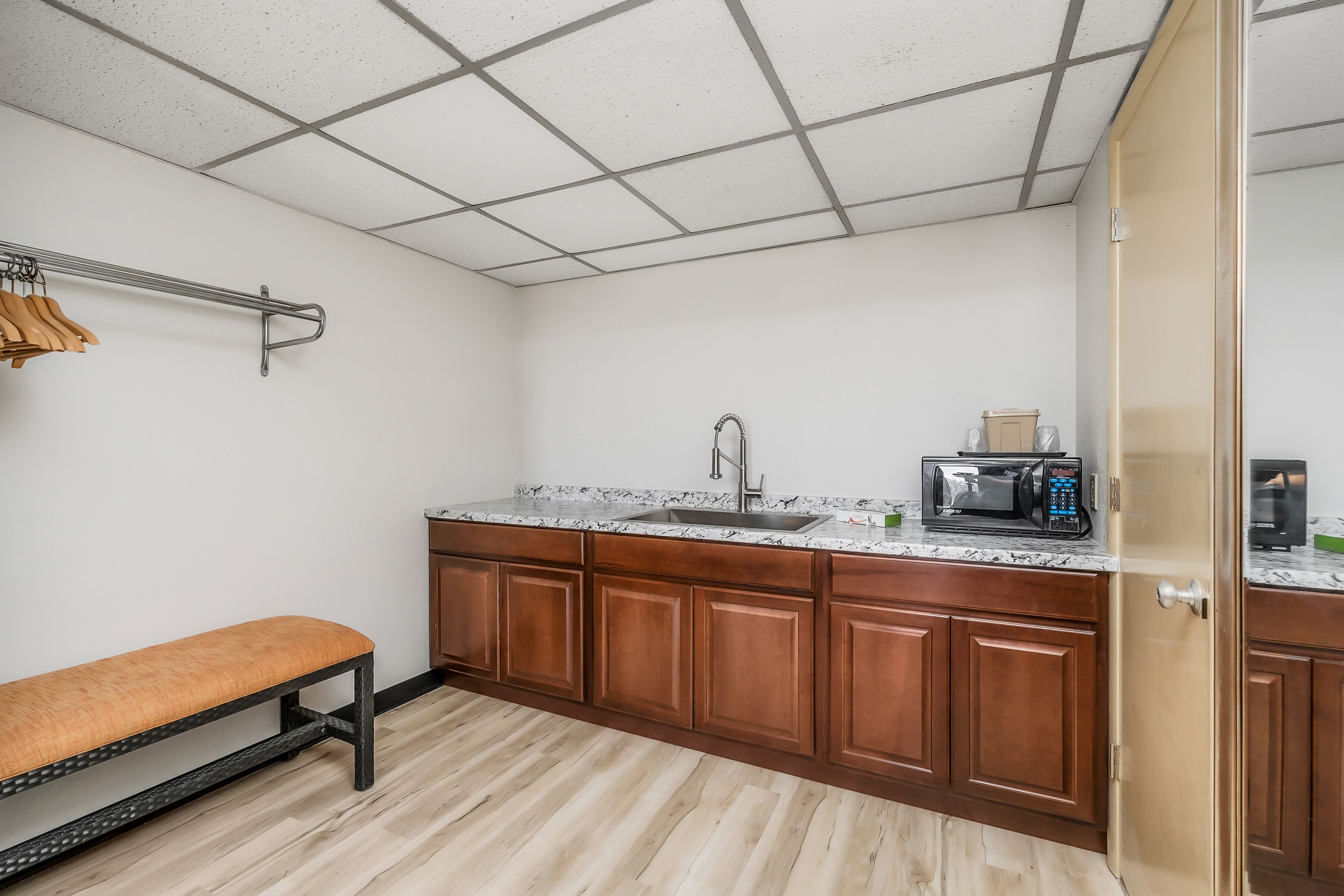 A kitchen with wooden cabinets, a marble countertop, a sink, a bench, and a microwave.