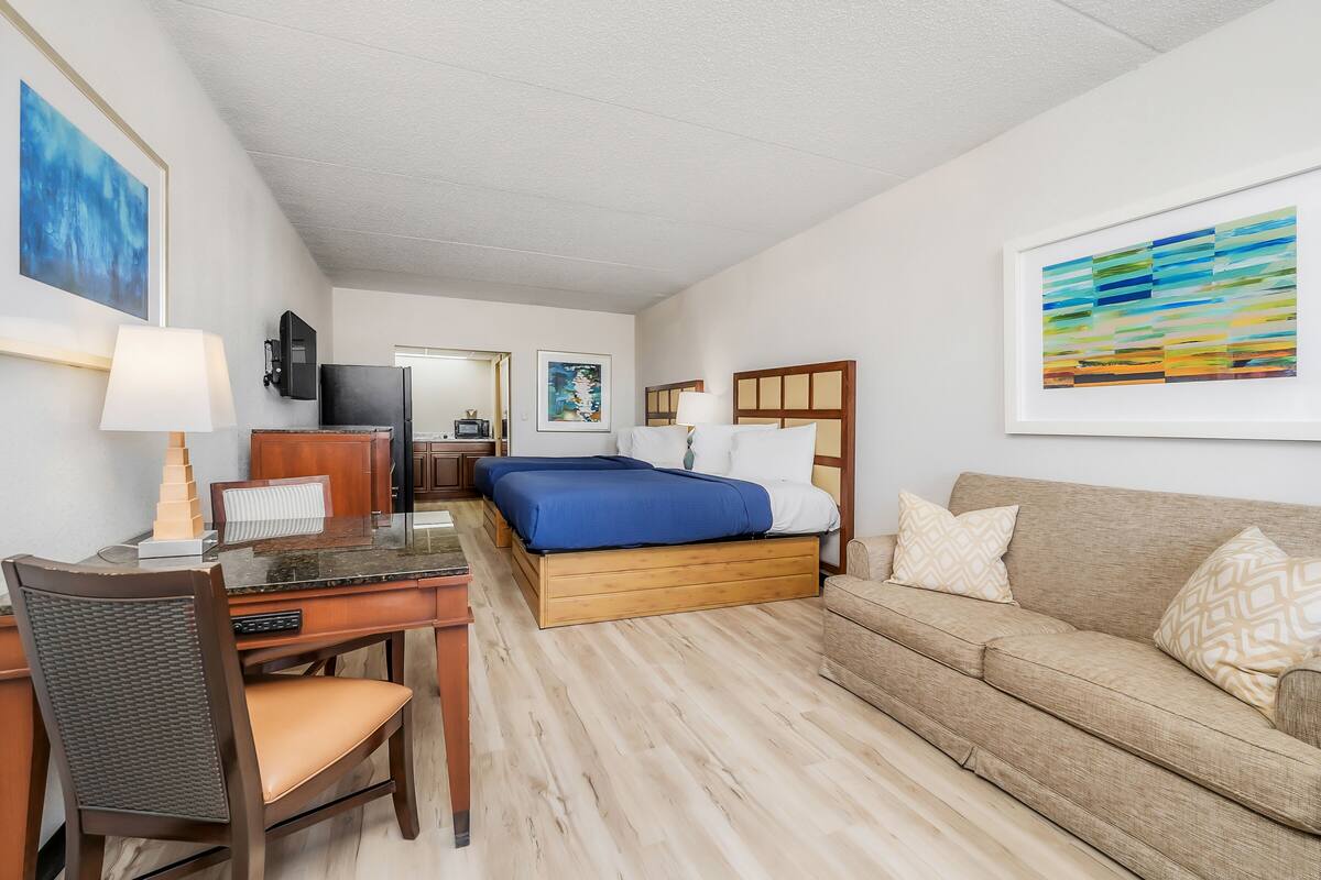 Une chambre d’hôtel avec un lit, un bureau, une chaise, un canapé et des œuvres d’art accrochées aux murs.