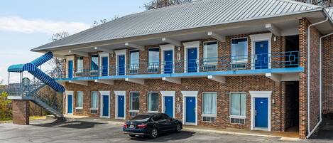 Um motel com fachada de tijolos, várias portas azuis e uma escadaria azul que leva a um andar superior.