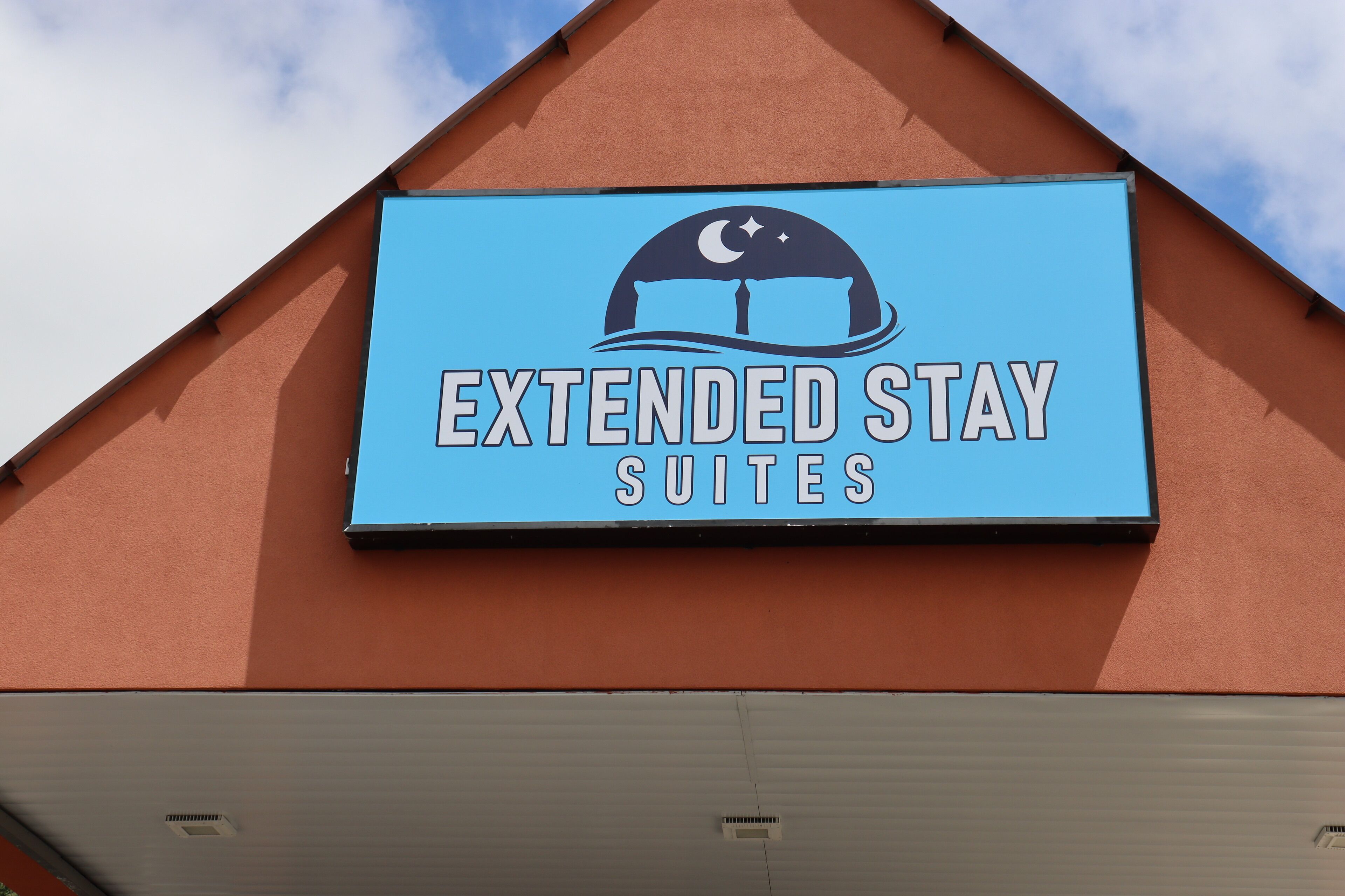 Une enseigne pour l’hôtel Extended Stay Suites, avec un logo représentant un croissant de lune et des étoiles.