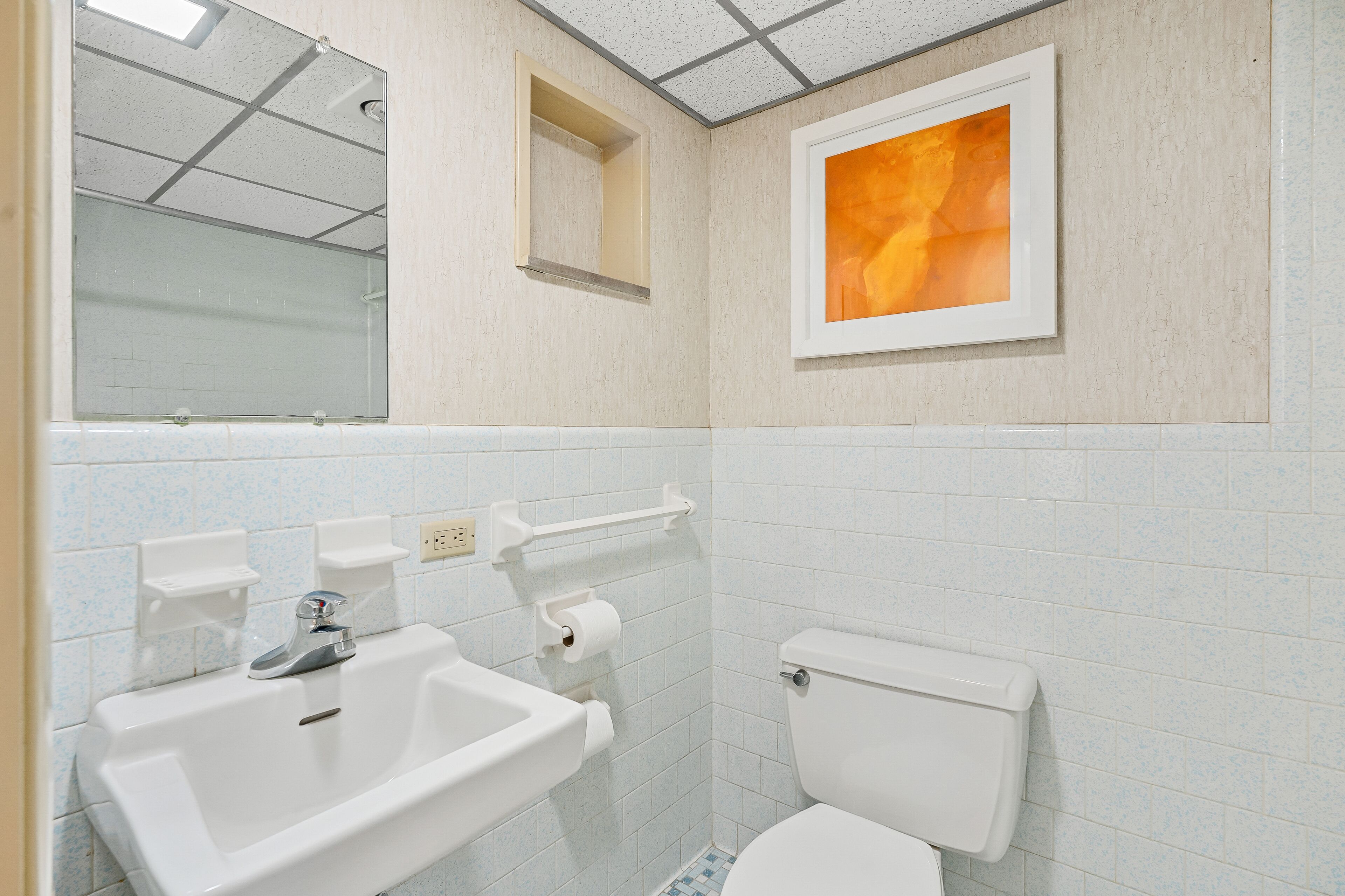 Casa de banho com lavatório, sanita e um quadro emoldurado na parede.