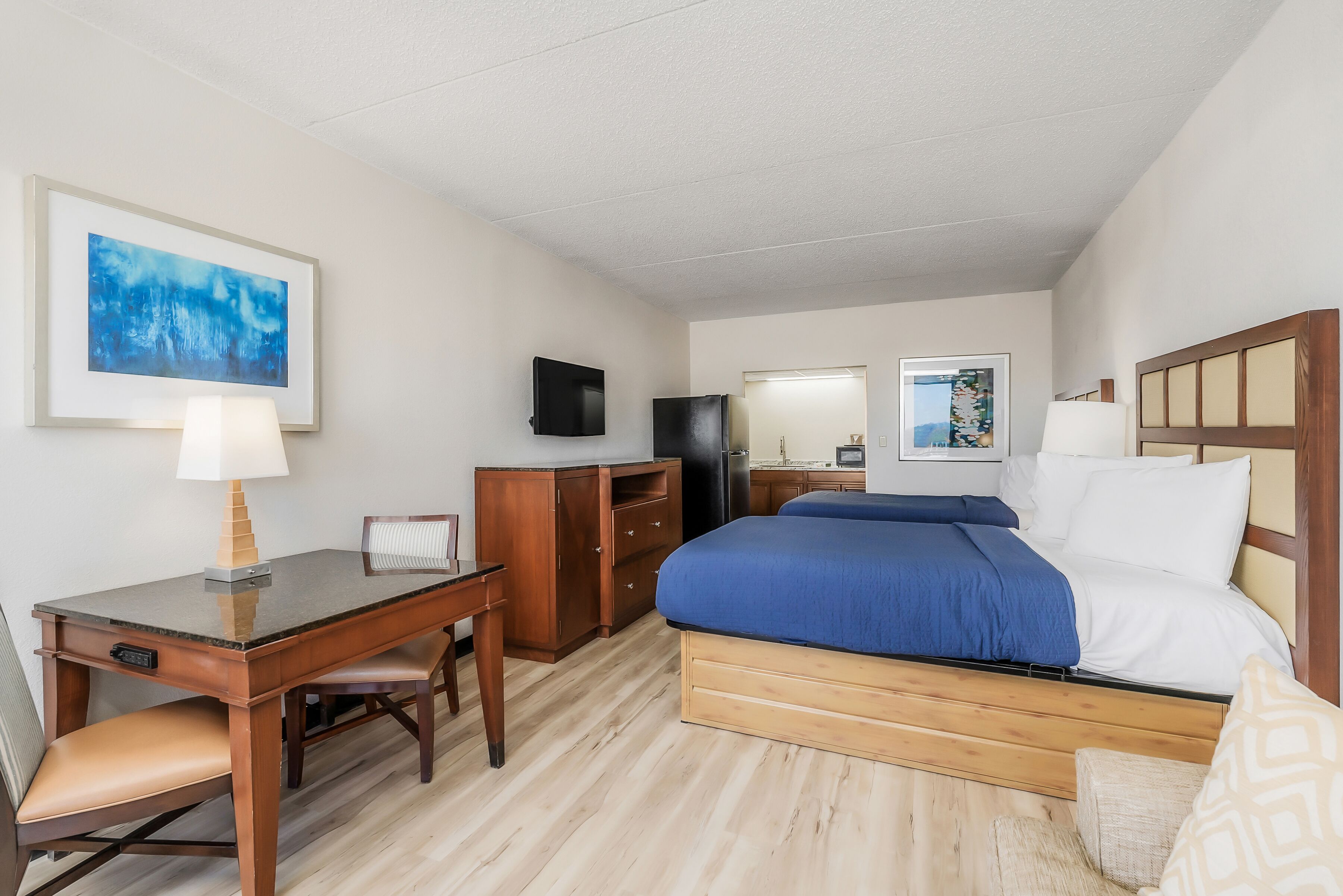 A hotel room with a bed, desk, chair, and a television.