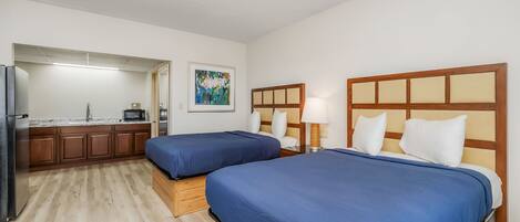 A hotel room with two beds, a kitchenette, and a painting on the wall.
