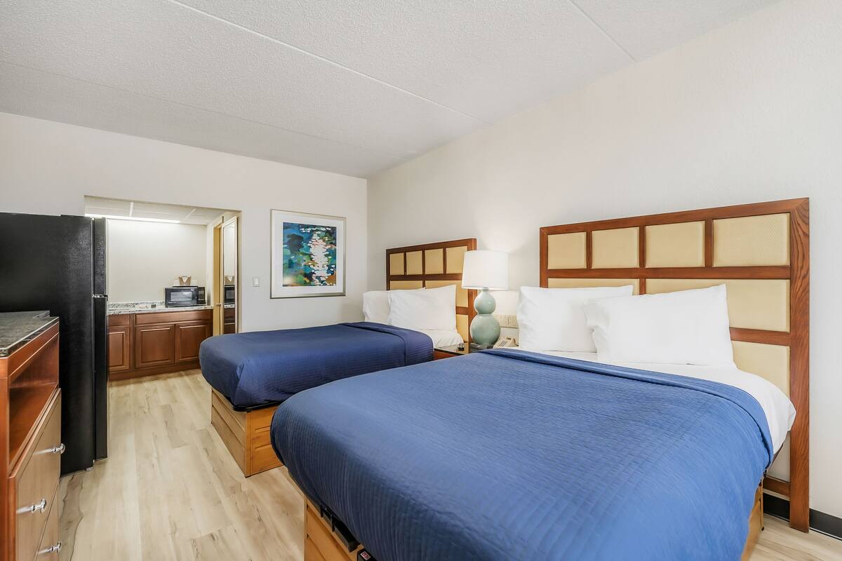 Une chambre d’hôtel avec deux lits, un coin cuisine, une télévision et un tableau au mur.