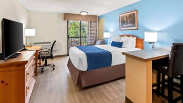 A hotel room with a bed, desk, chair, TV, and a view of the outdoors.